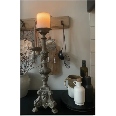 Antieke kerkelijke kandelaar met indrukwekkende details, een echte blikvanger voor een klassiek of rustiek interieur. Deze zware metalen kandelaar staat stevig op drie sierlijke pootjes en is versierd met florale motieven en een majestueuze leeuwenkop. Het bovenste gedeelte biedt ruimte voor een grote kaars, wat zorgt voor een warme, authentieke sfeer. Perfect als decoratiestuk of functioneel item in een sfeervolle woonruimte.