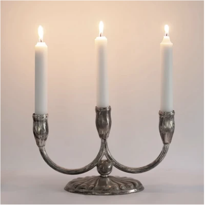 Deze vintage kandelaar met drie armen is uitgevoerd in verzilverd metaal en valt op door de sierlijke vorm en subtiele bewerking in het oppervlak. De zachte lijnen van de armen en de tulpvormige kaarshouders geven de kandelaar een klassieke uitstraling, terwijl de authentieke patina zorgt voor karakter en diepte. Waarschijnlijk afkomstig van de Duitse manufaktur Quist Esslingen (1895–1981), bekend om hun verzilverde objecten van hoge kwaliteit. Dit type kandelaar werd rond 1950 geproduceerd en combineert klassieke symmetrie met de modernere eenvoud van die tijd. Het kleine stempel aan de onderzijde wijst op de herkomst. Bij Noii HOME hebben we er bewust voor gekozen deze kandelaar niet op te poetsen. Het natuurlijke en prachtige patina laat zien dat dit een doorleefd stuk is met een eigen verhaal – en dat maakt hem uniek. Stylingtip van Noii HOME: Plaats deze kandelaar op een dressoir of in het midden van de eettafel en combineer met keramiek en glaswerk. Het zachte kaarslicht benadrukt het patina en zorgt voor een warme sfeer in de ruimte. productspecificaties vintage verzilverde kandelaar met drie armen: Kleur: zilver met patina Materiaal: verzilverd metaal Afmetingen: hoogte: 15 cm, breedte: 25 cm, voetbreedte: 14,5 cm Aantal armen: 3 Kaarshouders: diameter 2,5 cm, diepte 5 cm Type kaars: standaard dinerkaarsen (iets dikkere varianten of gebruik van een strookje aluminiumfolie of kaarshulsjes zorgen voor extra stevigheid) Herkomst: waarschijnlijk Quist, Esslingen (Duitsland), ca. 1950 Conditie: vintage, met authentieke patina Deze vintage kandelaar met drie armen is een sfeervolle en tijdloze toevoeging aan het interieur. Door de combinatie van klassieke vormen en mid-century eenvoud is het een uniek stuk dat geschiedenis en stijl samenbrengt.